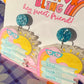 Close-up of the Total Book Worm teacher earrings showing the sun, bookworm and book-stack design