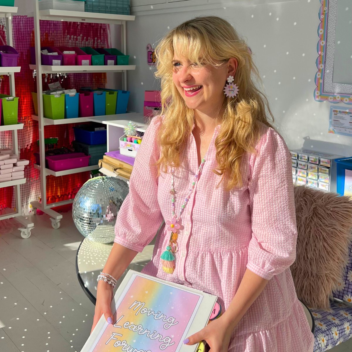 Teacher in a pink dress wearing a pastel beaded lanyard holding a educator binder in a classroom setting